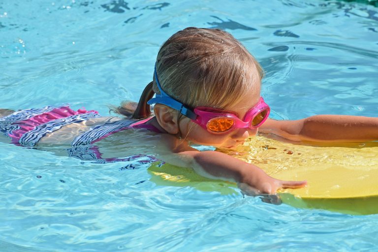 Little girl swimming in the pool with a flutter board and goggles.