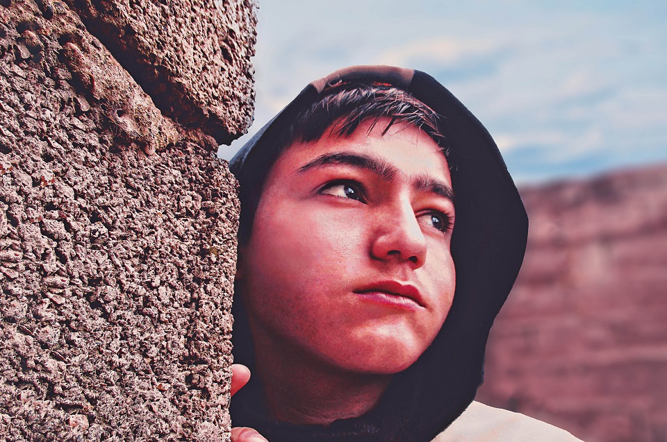 Hispanic teenage boy with a hoodie on, standing by rocks. Is he dealing with teenage problems?