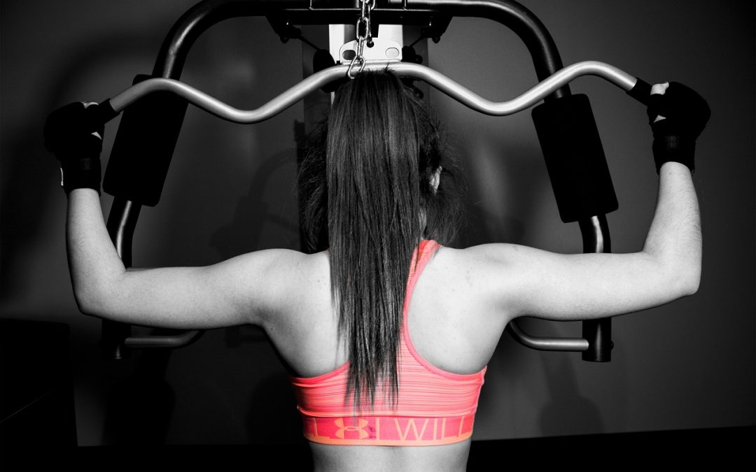 A physically fit woman is using gym equipment to build upper body strength as part of her Fitquest fitness routine.